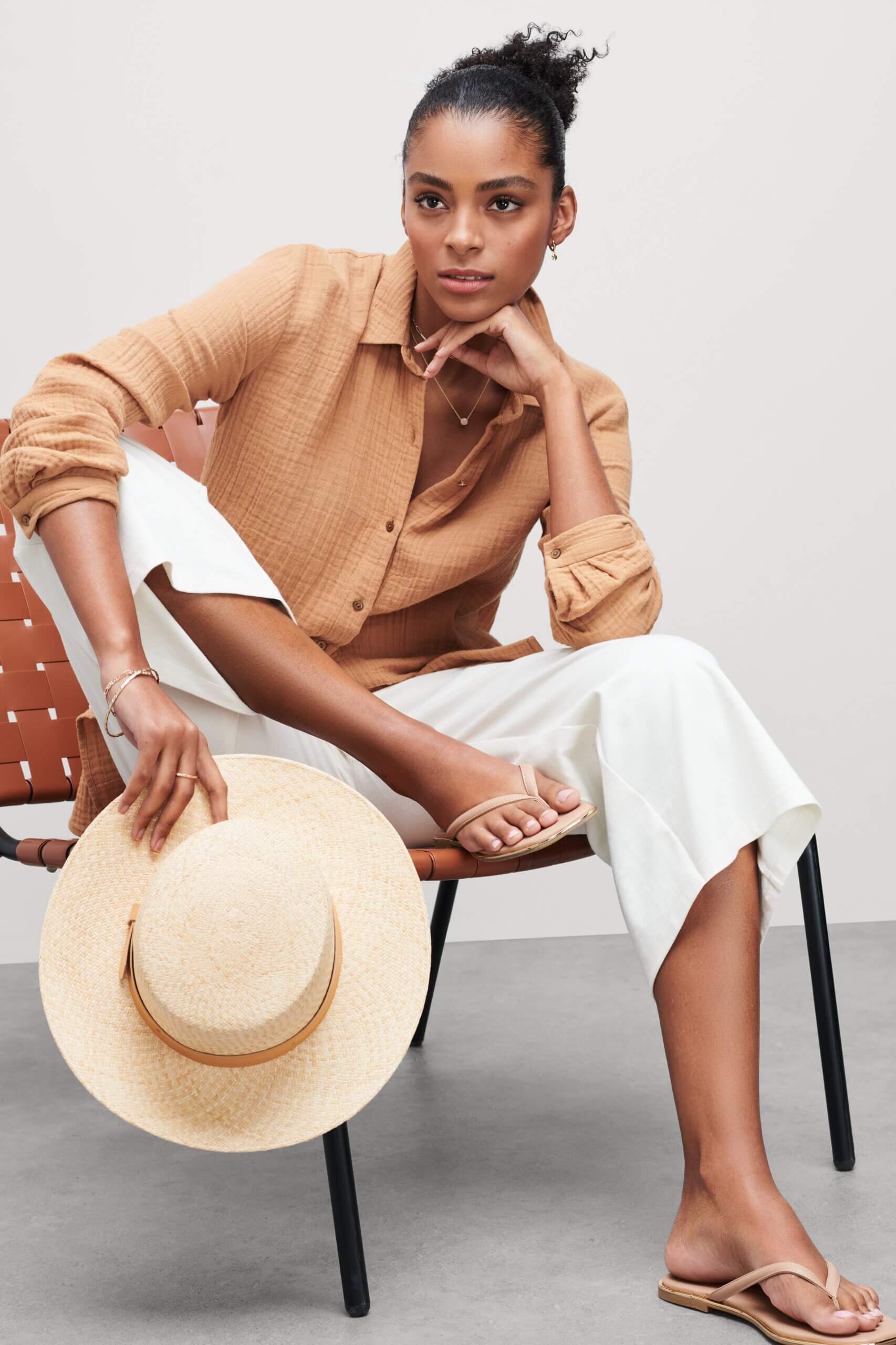 Stitch Fix model wearing women’s coastal grandmother outfit with white cropped pants, brown collared shirt, hat and sandals.