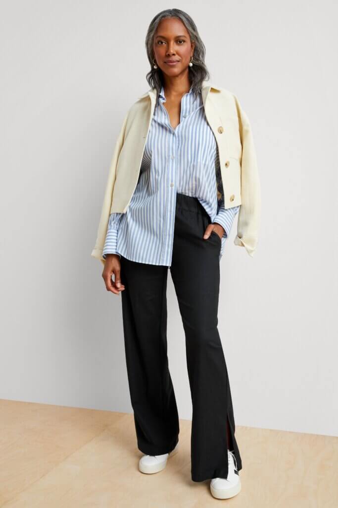 Stitch Fix model wearing women’s coastal grandmother outfit with black trousers, blue shirt, beige jacket, white sneakers.