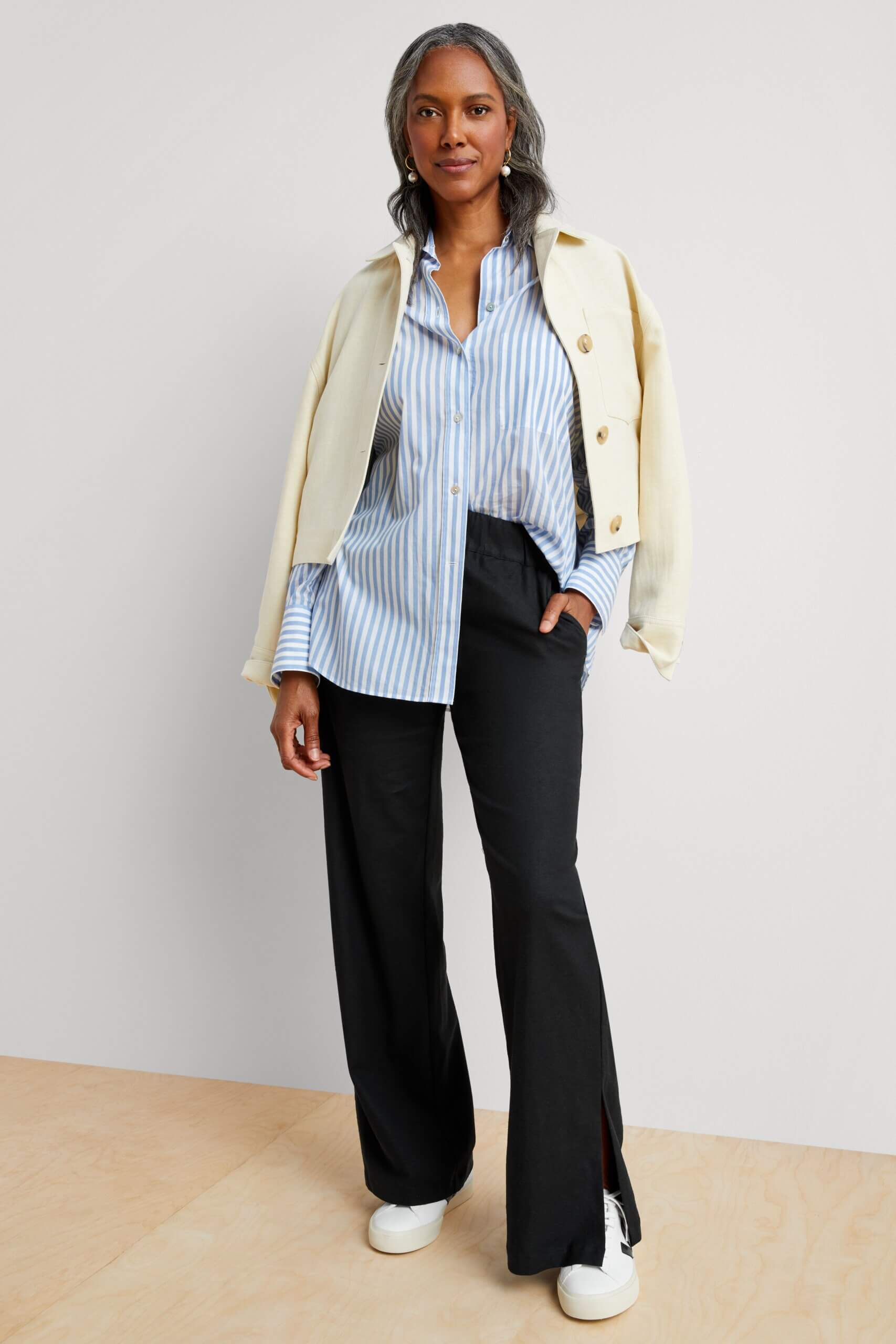 Stitch Fix model wearing women’s coastal grandmother outfit with black trousers, blue shirt, beige jacket, white sneakers.