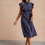 Stitch Fix women’s model wearing button-up accessorized navy blue dress for a wedding with brown sandals and gold bracelet.