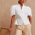Stitch Fix model wearing women’s cottagecore aesthetic outfit with white puff-sleeve blouse, khaki shorts and coral earrings.