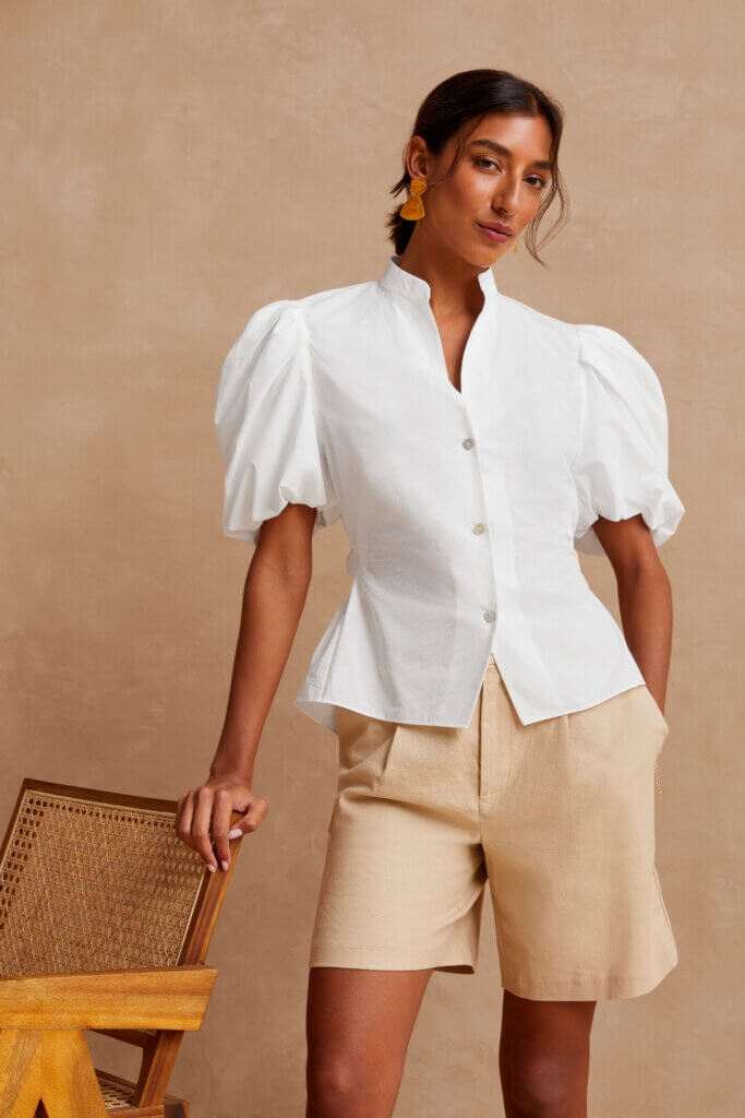 Stitch Fix model wearing women’s cottagecore aesthetic outfit with white puff-sleeve blouse, khaki shorts and coral earrings.