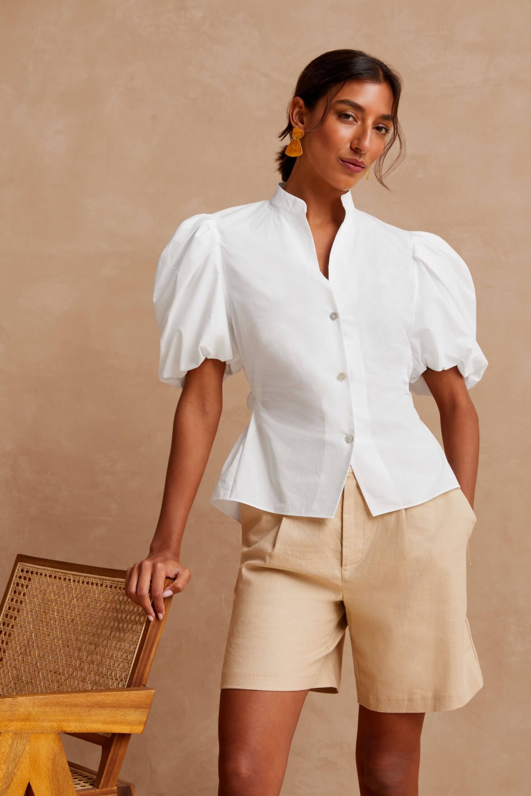 Stitch Fix model wearing women’s cottagecore aesthetic outfit with white puff-sleeve blouse, khaki shorts and coral earrings.