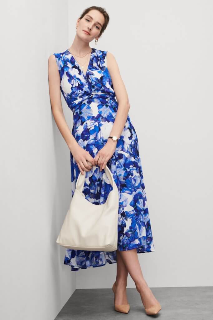 Stitch Fix women’s model wearing floral accessorized navy blue dress for a wedding with purse, watch, necklace and earrings.