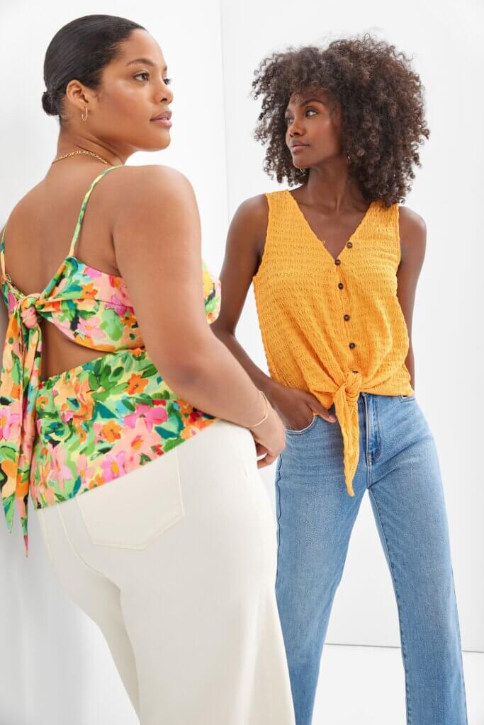 Two women stand in summer outfits: bright floral tops and denim bottoms.