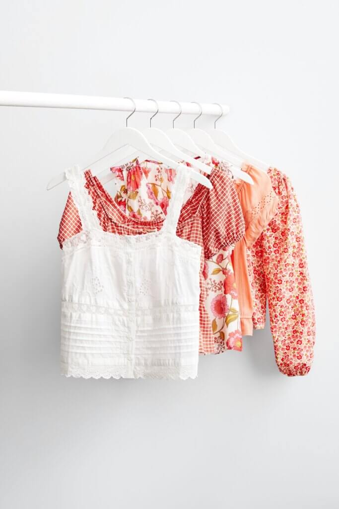 White, red, coral, melon and peach colored women’s summer tops hanging in a closet.