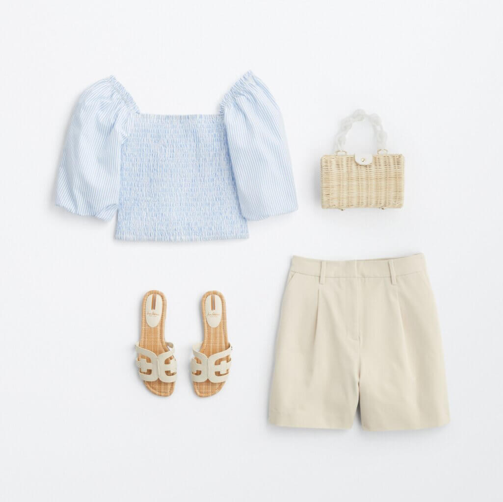 Top view of summer clothing: a light blue feminine top, chino shorts, slip-on sandals and a woven bag