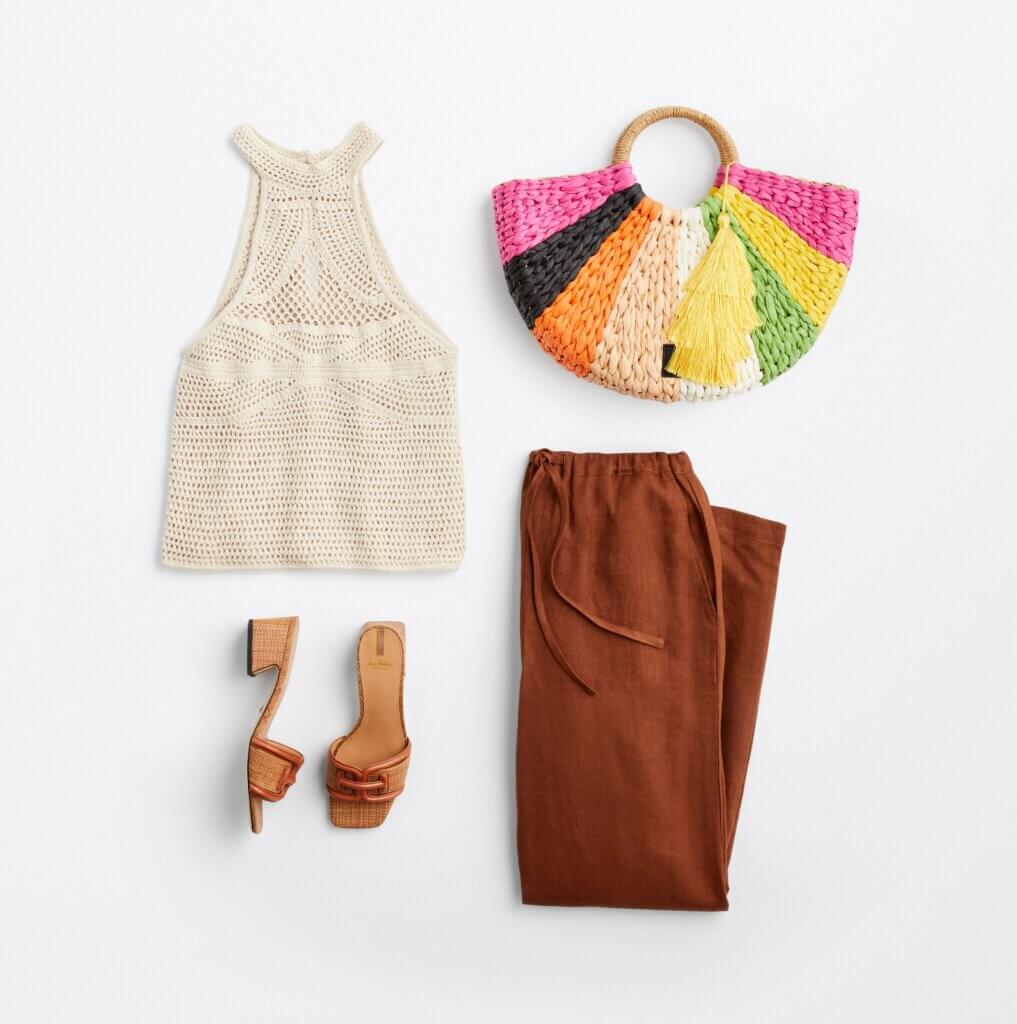 Top view of summer clothing: natural fabric top, a colorful woven handbag, brown slip-on sandals and brown elastic-waist pants.