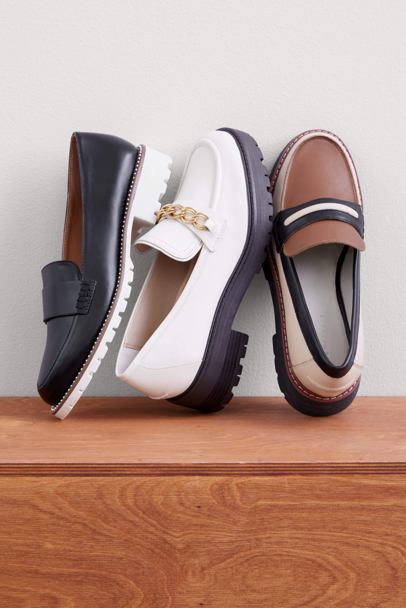 Three unpaired loafers on a wooden surface resting against a white wall. 